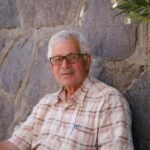 Portrait of an elderly man sitting against a stone wall outdoors in İzmir, Türkiye.